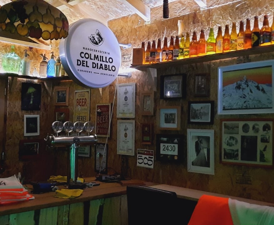 Barra del tour cervecero con el letrero de Colmillo del Diablo y botellas iluminadas